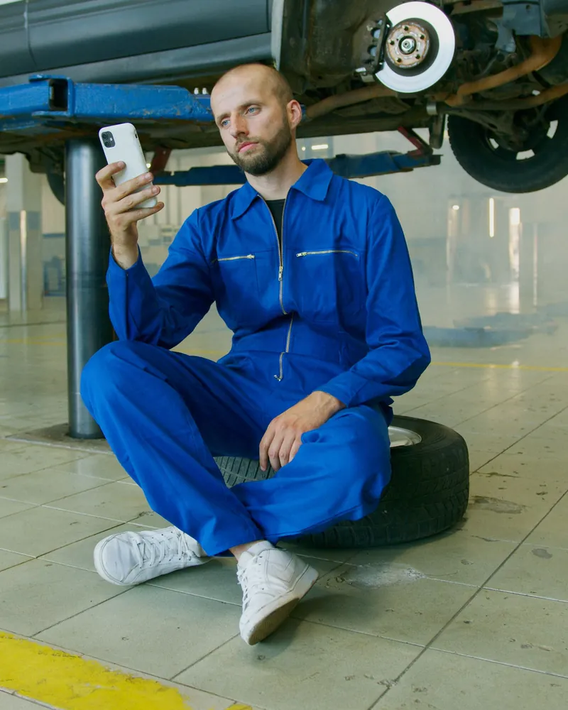 Mekaniker sidder på et dæk i værkstedet og kigger på sin telefon